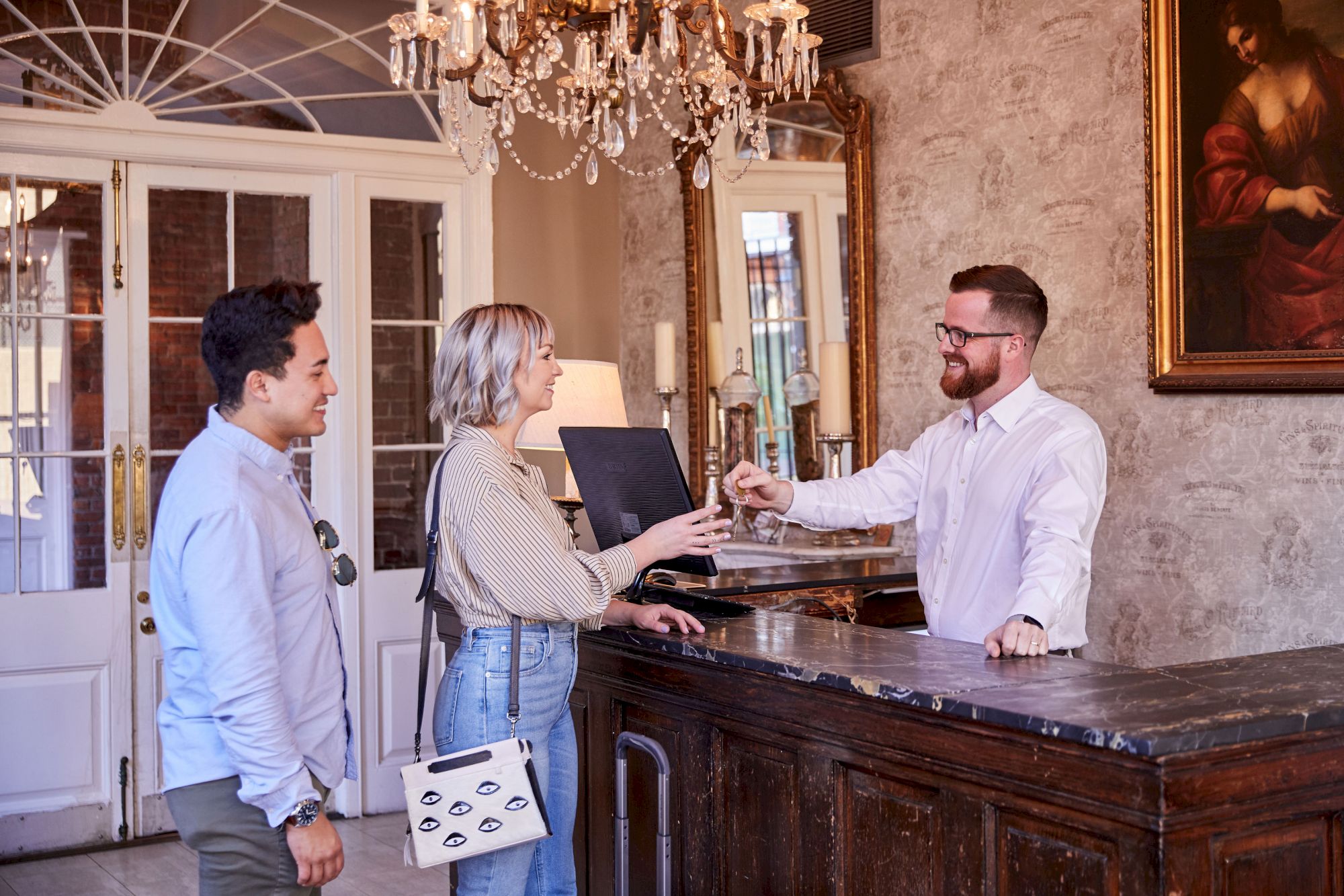 Three people at a reception desk; one is a receptionist handing something to a woman, with a man standing beside her.