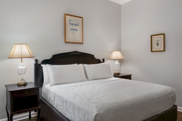 A neatly made bed with white linens, two bedside tables with lamps, and framed artwork above, all in a softly lit, neutral-toned room.