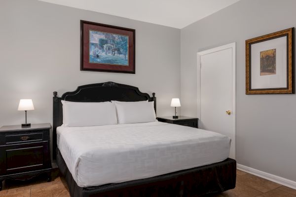 A neatly made bed with white linens and two bedside tables, each with a lamp, in a room with two framed artworks on gray walls.