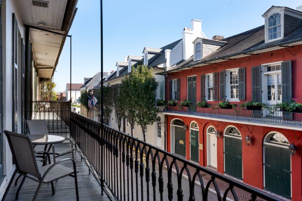 A balcony with chairs overlooks colorful, historic buildings and a tree-lined street in a charming neighborhood.