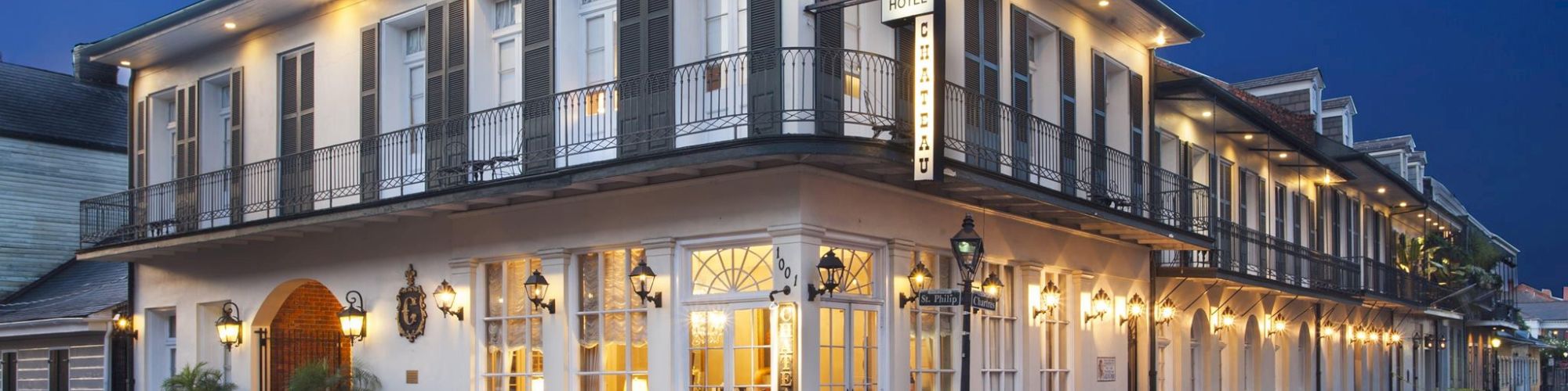 A well-lit, two-story building with balconies and large windows on a quiet street corner during evening.