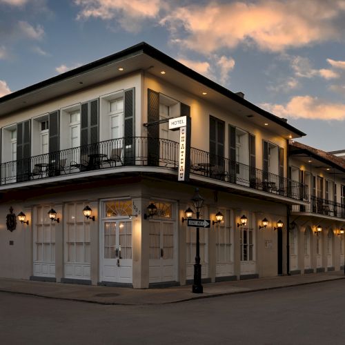 A historic building with balconies at dusk, featuring lanterns and a corner street sign, under a sky with scattered clouds.