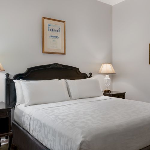 A neatly arranged bedroom with a bed, two side tables with lamps, and framed artwork on light gray walls.