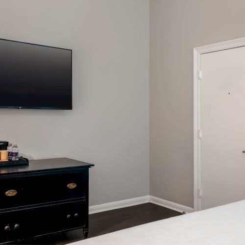 A minimalist room with a wall-mounted TV, black dresser with coffee maker, and a closed white door with a modern handle.