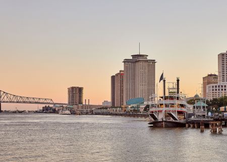 Riverfront view with a bridge, high-rise buildings, and a docked riverboat at sunset in the cityscape.