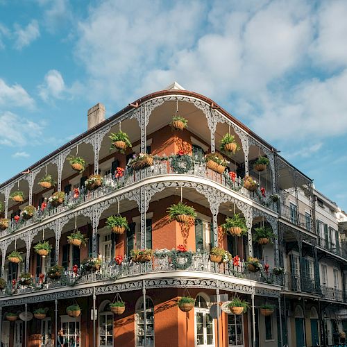 The image features a historic building with ornate ironwork balconies adorned with hanging plants against a partly cloudy sky.