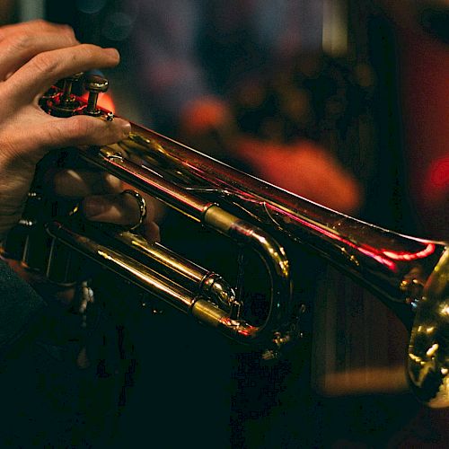 A person playing a brass trumpet, with a warm, dimly lit background, capturing the ambiance of a live music performance.