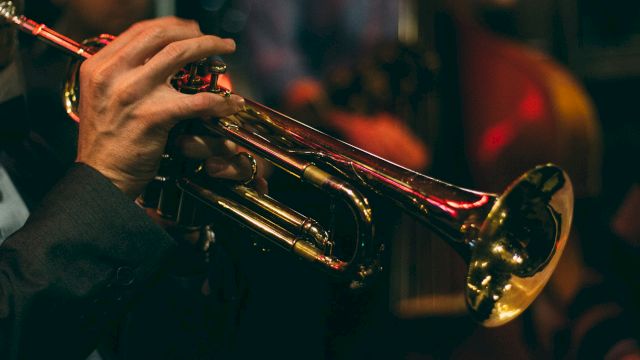 A person playing a brass trumpet, with a warm, dimly lit background, capturing the ambiance of a live music performance.