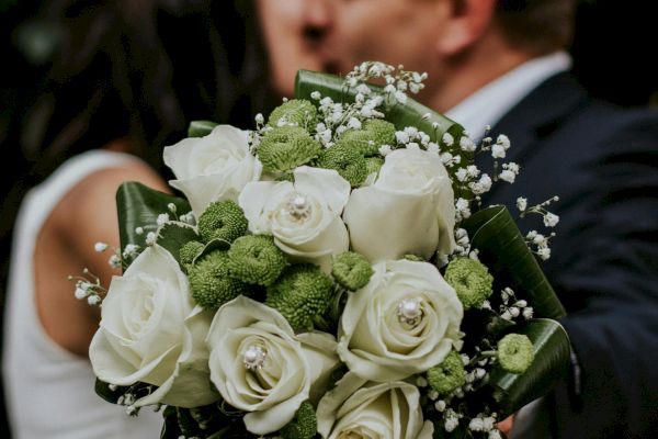 A couple is kissing, with a focus on a bouquet of white and green flowers in the foreground, creating a romantic scene.