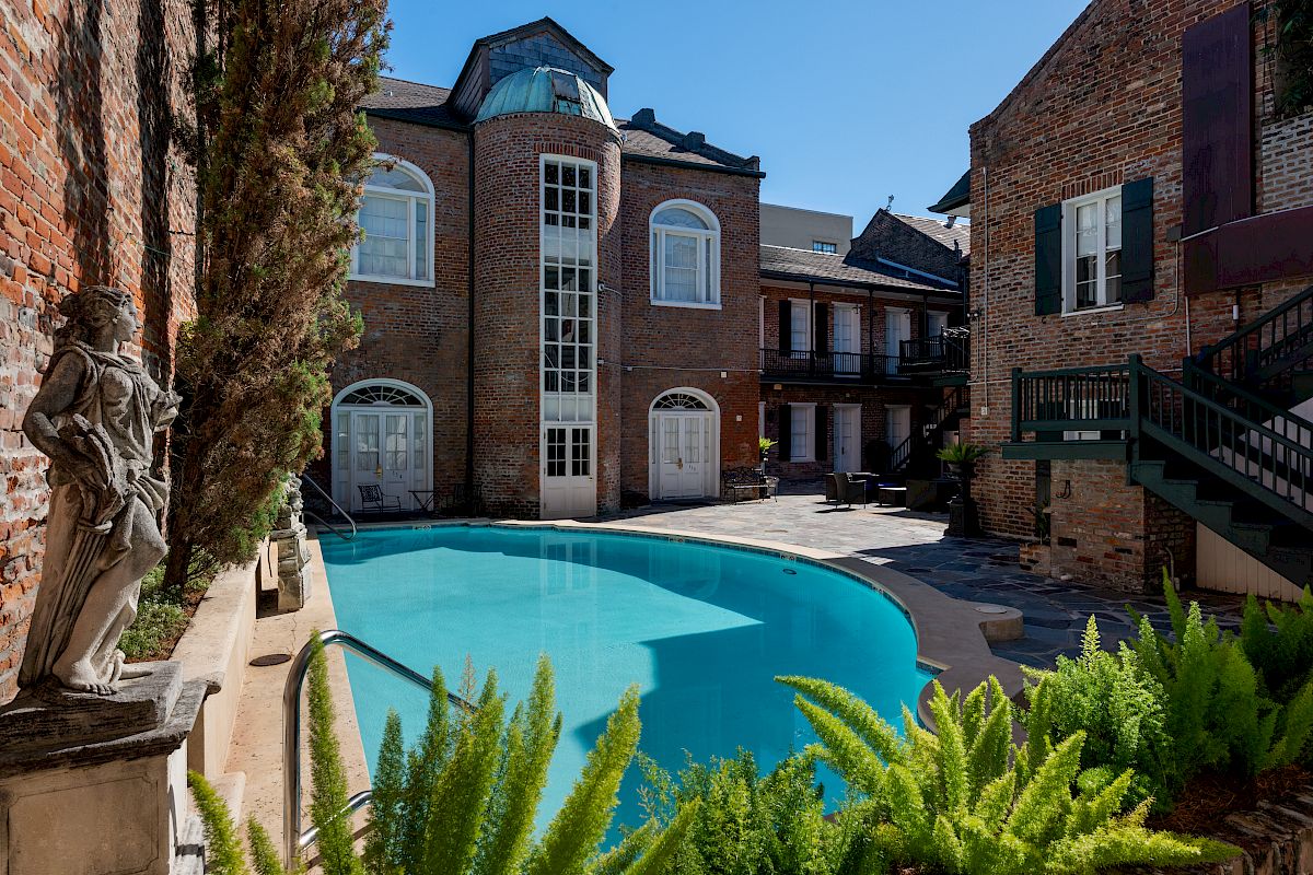 A charming courtyard features a curved swimming pool, surrounded by brick buildings and greenery, with a statue by the poolside.