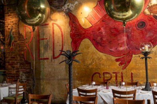 A restaurant interior with decorated tables, gold balloons, and a mural of a red fish on the wall, creating a festive atmosphere.