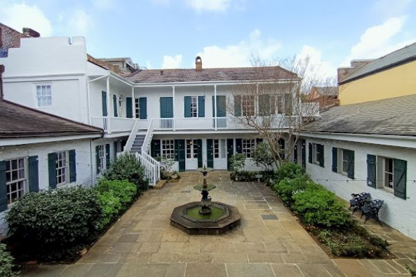 The image shows a courtyard with a central fountain, surrounded by a two-story building with doors and windows.