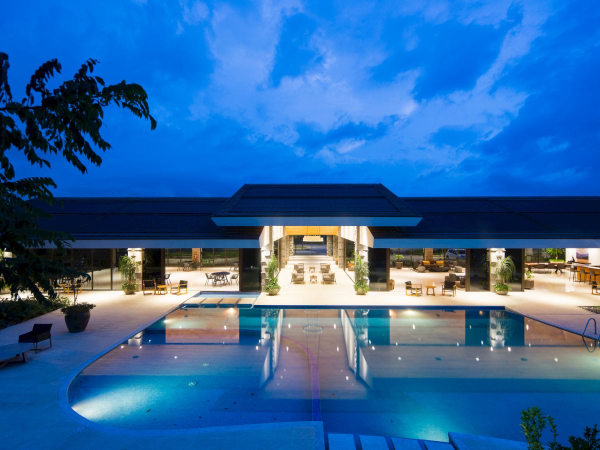 Luxurious pool at twilight with lights and a modern building in the background.